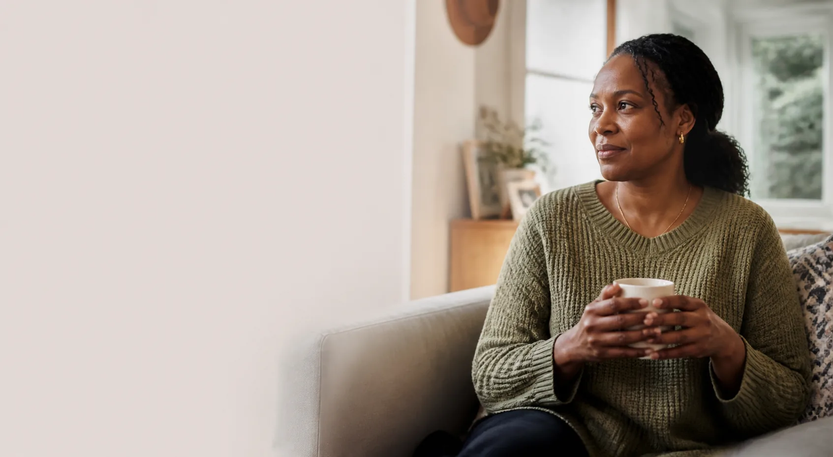 A Black woman pausing with a mug in a warmly lit living room
